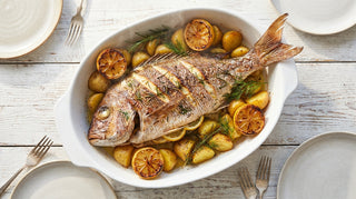 Whole roasted snapper on a tray with lemon slices, potatoes and herbs