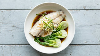 Steamed barramundi fillet topped with ginger and spring onion beside bok choy