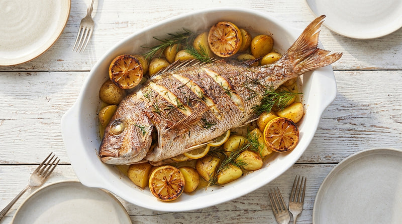 Whole roasted snapper on a tray with lemon slices, potatoes and herbs